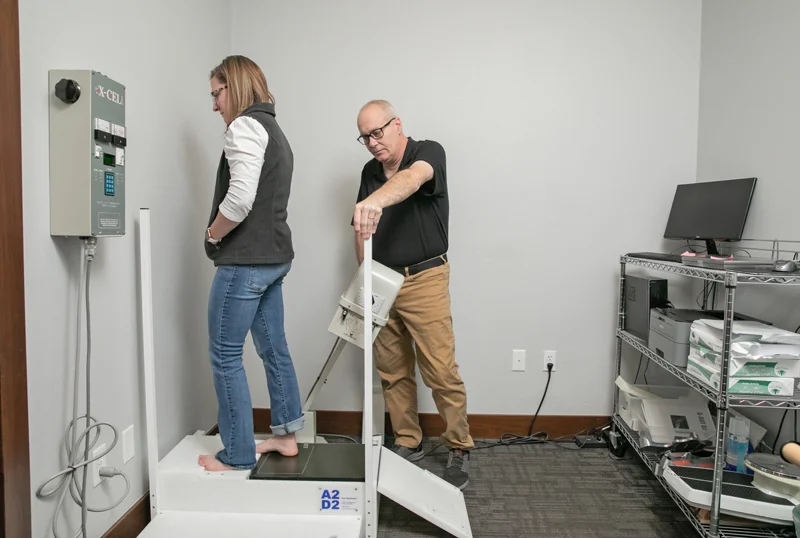 Healthcare professional assisting a patient standing on an examination platform during a clinical evaluation.